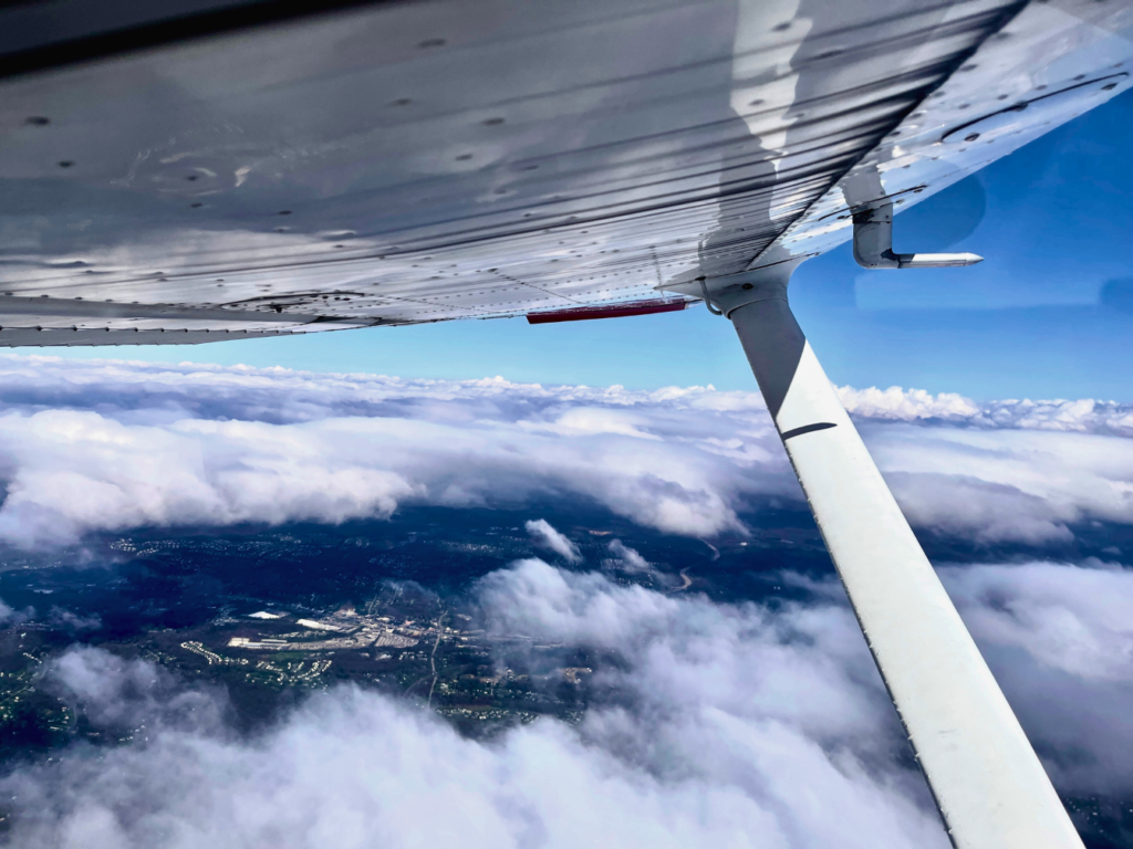 High Flight Academy's plane maintenance team keeps our fleet of Cessna 172s, Piper Warriors, and a Piper Seneca airworthy like this Cessna in flight above the clouds on with the sky bright blue all around.